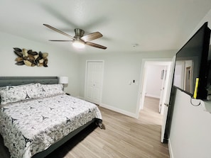 A bedroom with a bed, a ceiling fan, a door, and a mirror.