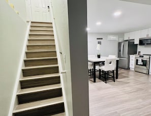 A modern kitchen with a central island, stainless steel appliances, and a dining area with white chairs.