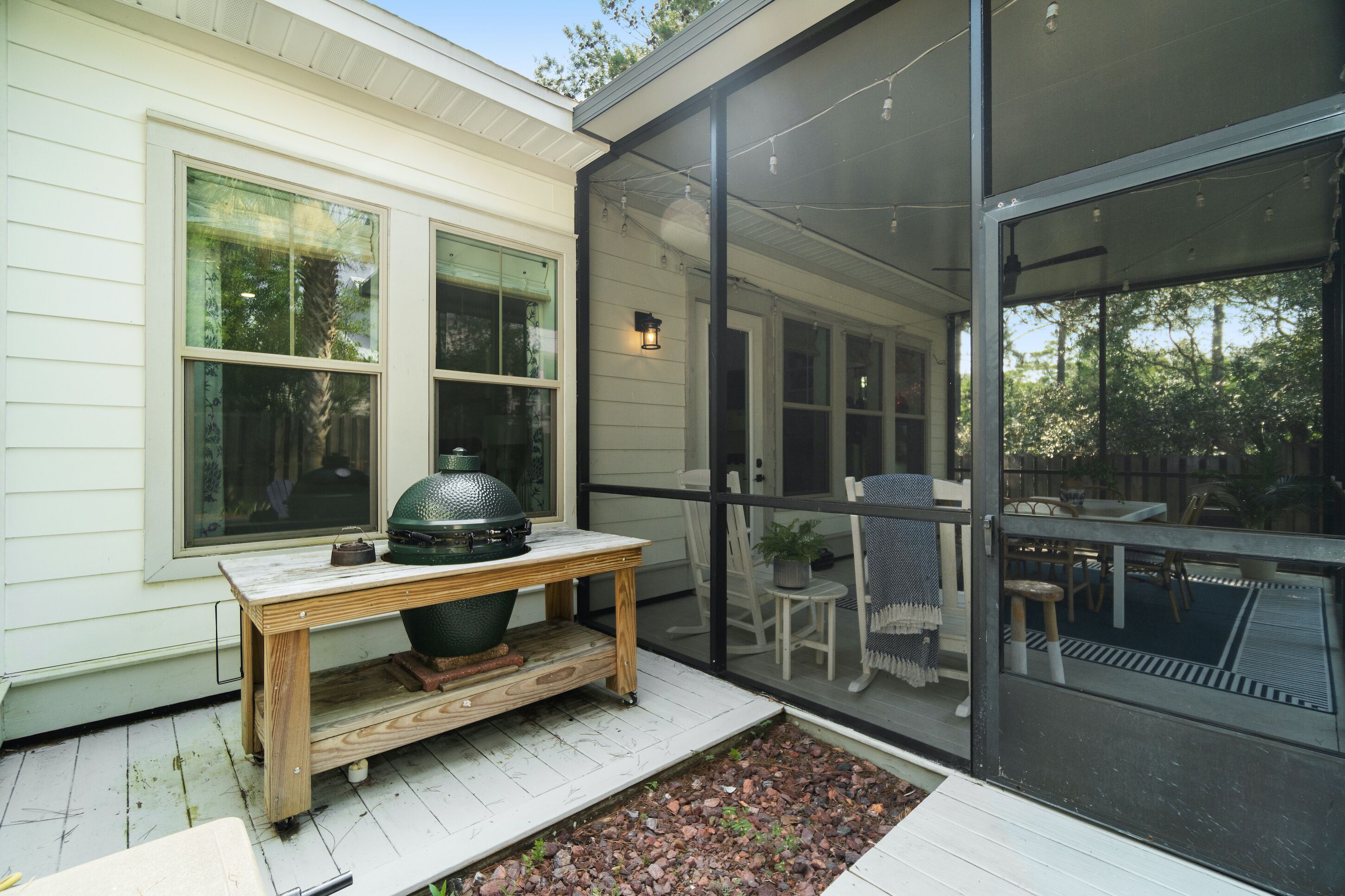 A covered outdoor patio with a wooden table and a large grill, surrounded by chairs and a dining table.