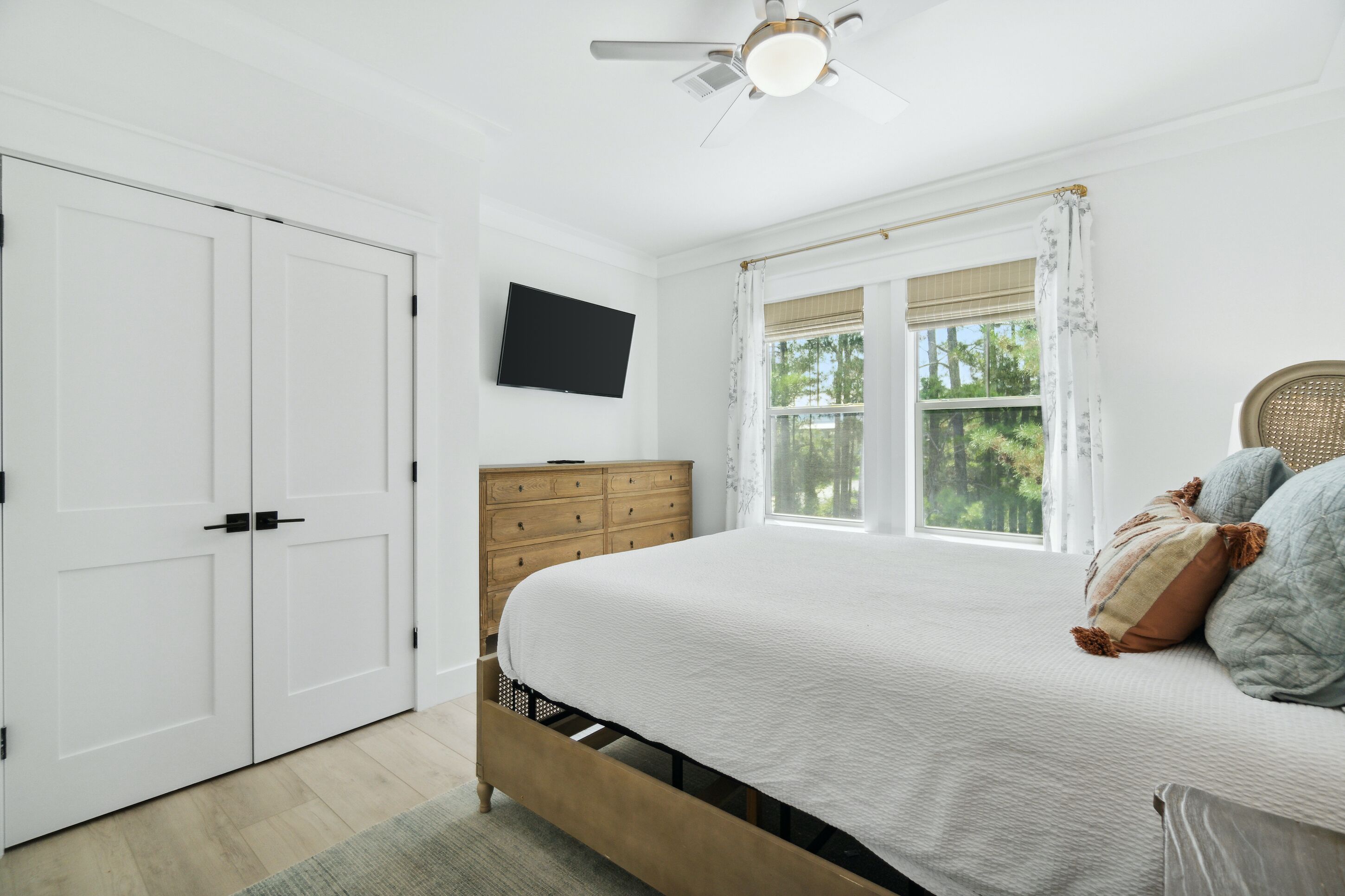 Une chambre à coucher avec un lit, une commode en bois, un téléviseur et une fenêtre avec des rideaux.