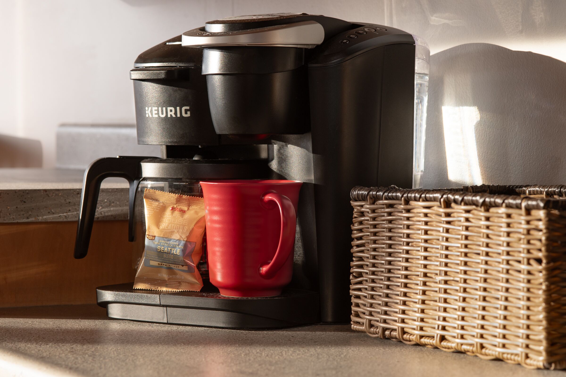 A Keurig coffee maker with a red mug and a coffee pod on a kitchen counter next to a wicker basket.