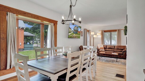 A dining area with a wooden table and chairs, a chandelier, and a view of a house through large windows. - -RARE- In-Village rental! 4-Bedrooms w HOT TUB & AC
 (Ellicottville)