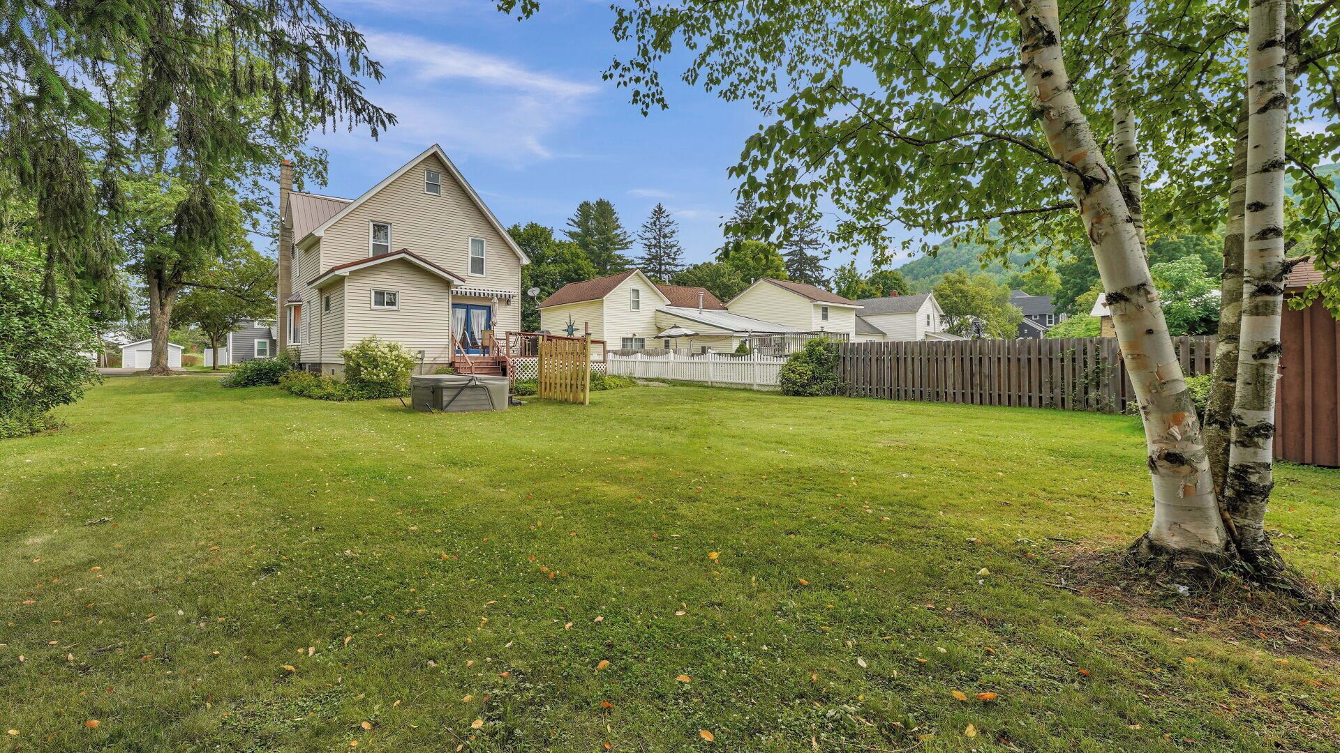 A residential area with a large house, a fenced yard, and a tree.