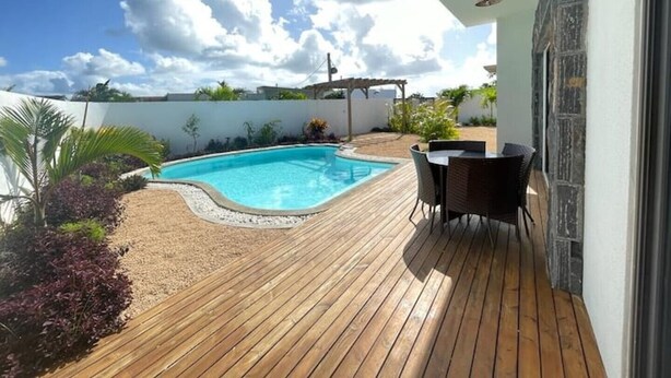 A wooden deck with a swimming pool, outdoor furniture, and a pergola.