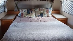 A bedroom with a bed, wooden headboard, two nightstands, a window with curtains, and a ceiling light. - Camp Lilybug-Calm Oasis Pet Friendly! (Terre Haute)