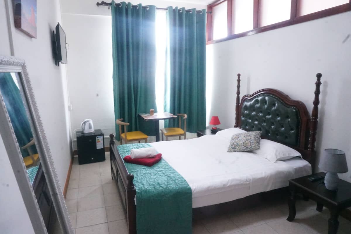 Una habitación de hotel con cama, escritorio, silla, lámpara y espejo.