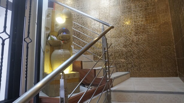 Una escalera con barandilla metálica, un muro decorativo con diseños circulares y una lámpara en la pared.