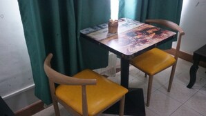 Una pequeña mesa de comedor con dos sillas, un objeto decorativo sobre la mesa y cortinas verdes al fondo.
