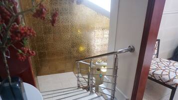 Una escalera con barandilla de metal, un muro con diseño y una silla con cojín geométrico.