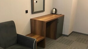 Un espacio de oficina moderno con un sofá gris oscuro, un escritorio de madera y una cafetera.