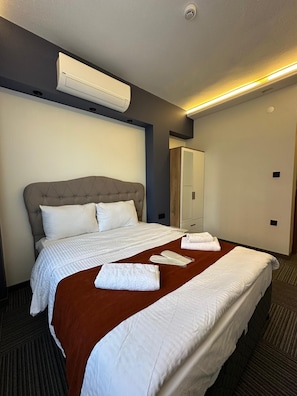 A hotel room with a large bed, a wardrobe, and a ceiling-mounted air conditioner.