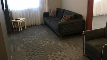 A hotel room with a dark grey sofa, a small wooden side table, and a patterned throw pillow.