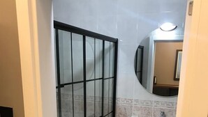 Un baño con puerta de cristal, lavamanos y espejo.