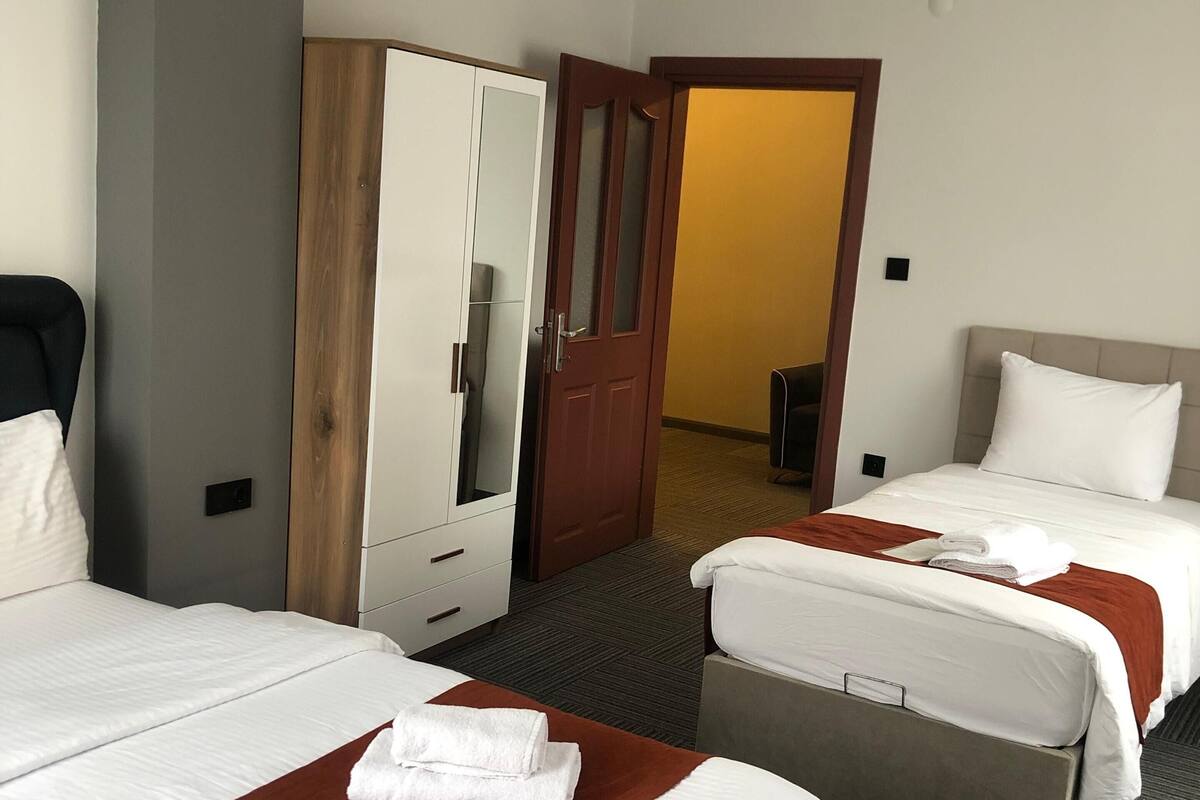 Quarto de hotel com duas camas, um guarda-roupa e uma porta que dá para outro espaço.