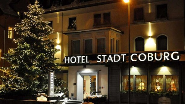 Hoteleingang mit Weihnachtsbaum und einem Schild, auf dem 'HOTEL STADT COBURG' steht.