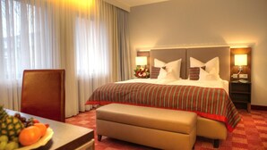 Ein Hotelzimmer mit einem großen Bett, einem Holzkopfende, einem Nachttisch mit Lampe, einem Sessel und einem kleinen Tisch mit Obst.