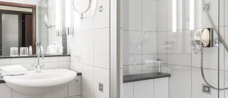 A modern bathroom with a white sink, a mirror, and a glass-enclosed shower area.