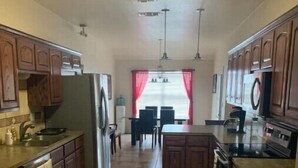 Una cocina con armarios de madera, una isla central, un refrigerador y una zona de comedor con sillas y una mesa.