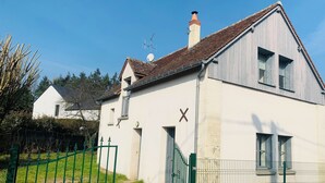 A white building with a sloped roof and a chimney, a green gate, and a clear sky.