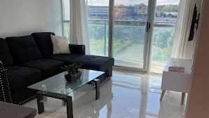 A modern living room with a black sofa, a glass coffee table, and a large window with curtains. - Lovely 1 bedroom unit with balcony. Sleeps 1-4 (Whitby)