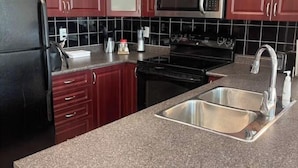 A kitchen with dark red cabinets, a black refrigerator, a stainless steel sink, a microwave, and a stove. - Lovely 1 bedroom unit with balcony. Sleeps 1-4 (Whitby)