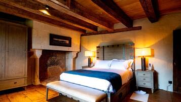 Une chambre confortable avec un plancher en bois, un lit recouvert d’une couverture bleue, un banc et une table de chevet avec une lampe.