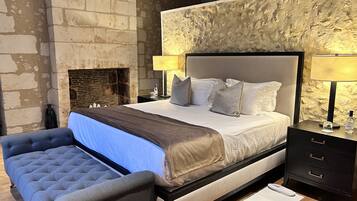 A bedroom with a large bed, a fireplace, a nightstand, and a chair.