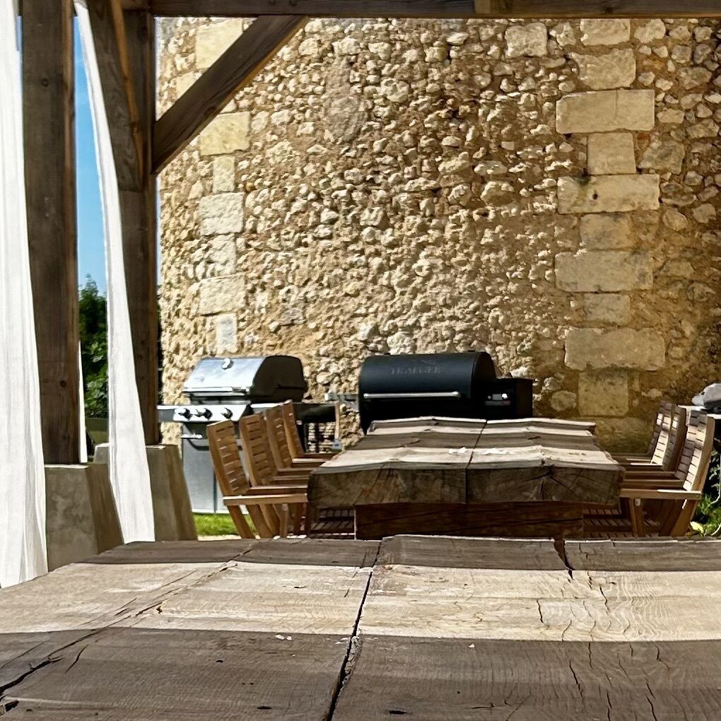 An outdoor patio with stone walls, a grill, and wooden furniture.