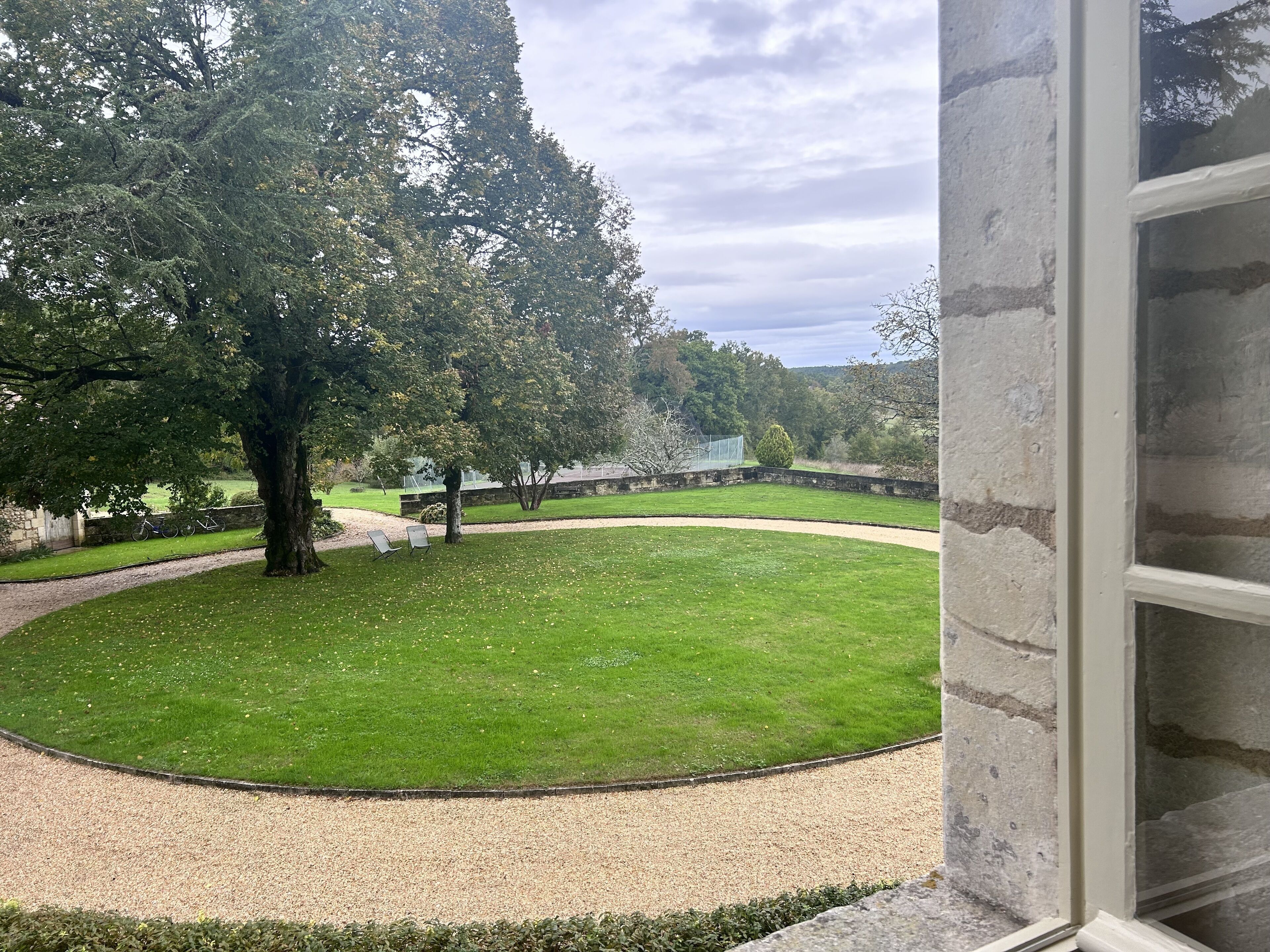 A view of a well-maintained lawn with a large tree, a gravel path, and a stone wall.