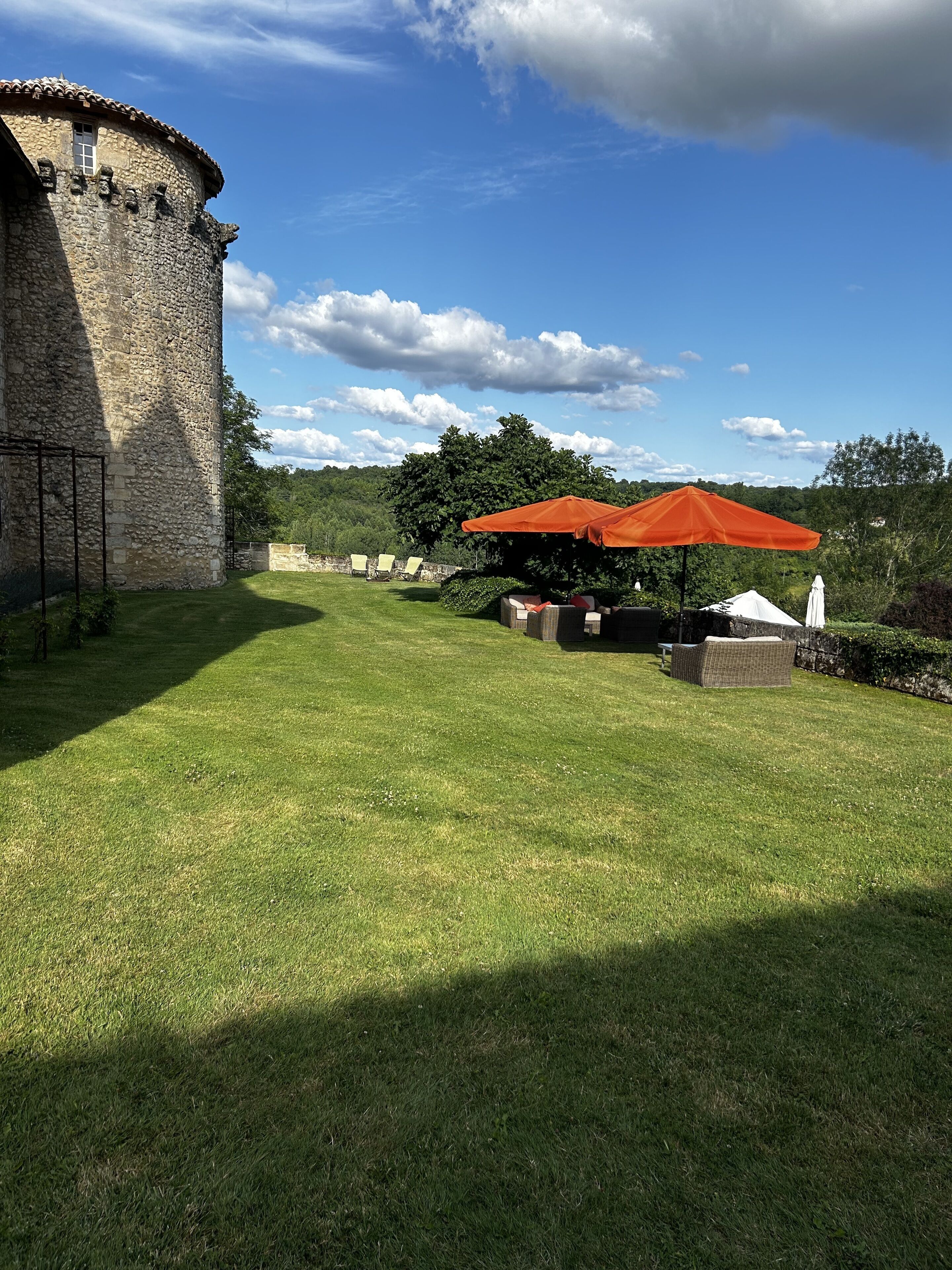 A stone tower, a grassy lawn, outdoor seating with an orange umbrella, and a white tent.