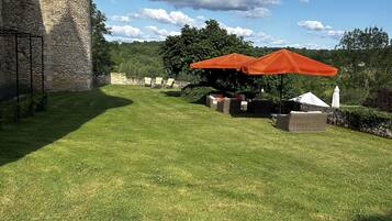 A stone tower, a grassy lawn, outdoor seating with an orange umbrella, and a white tent.