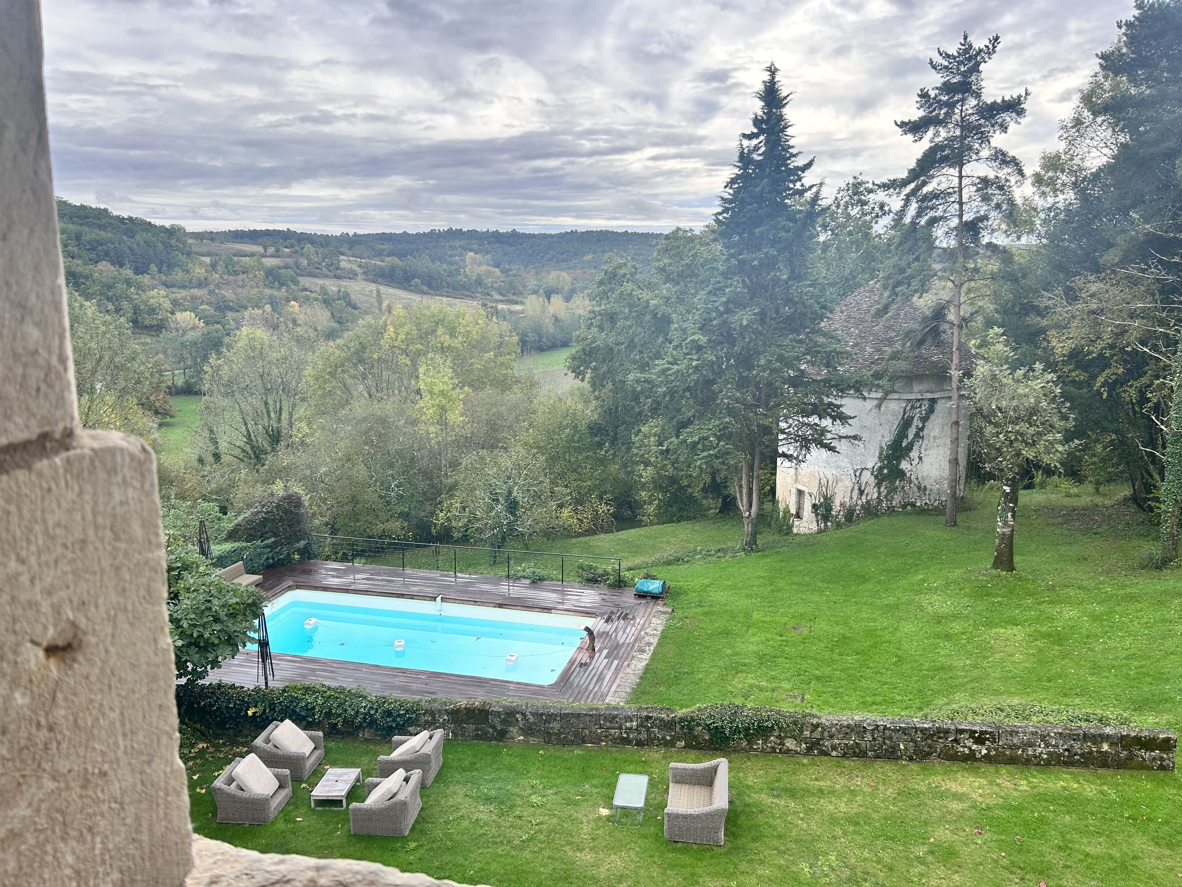 A pool with a wooden deck, surrounded by a grassy lawn and trees.