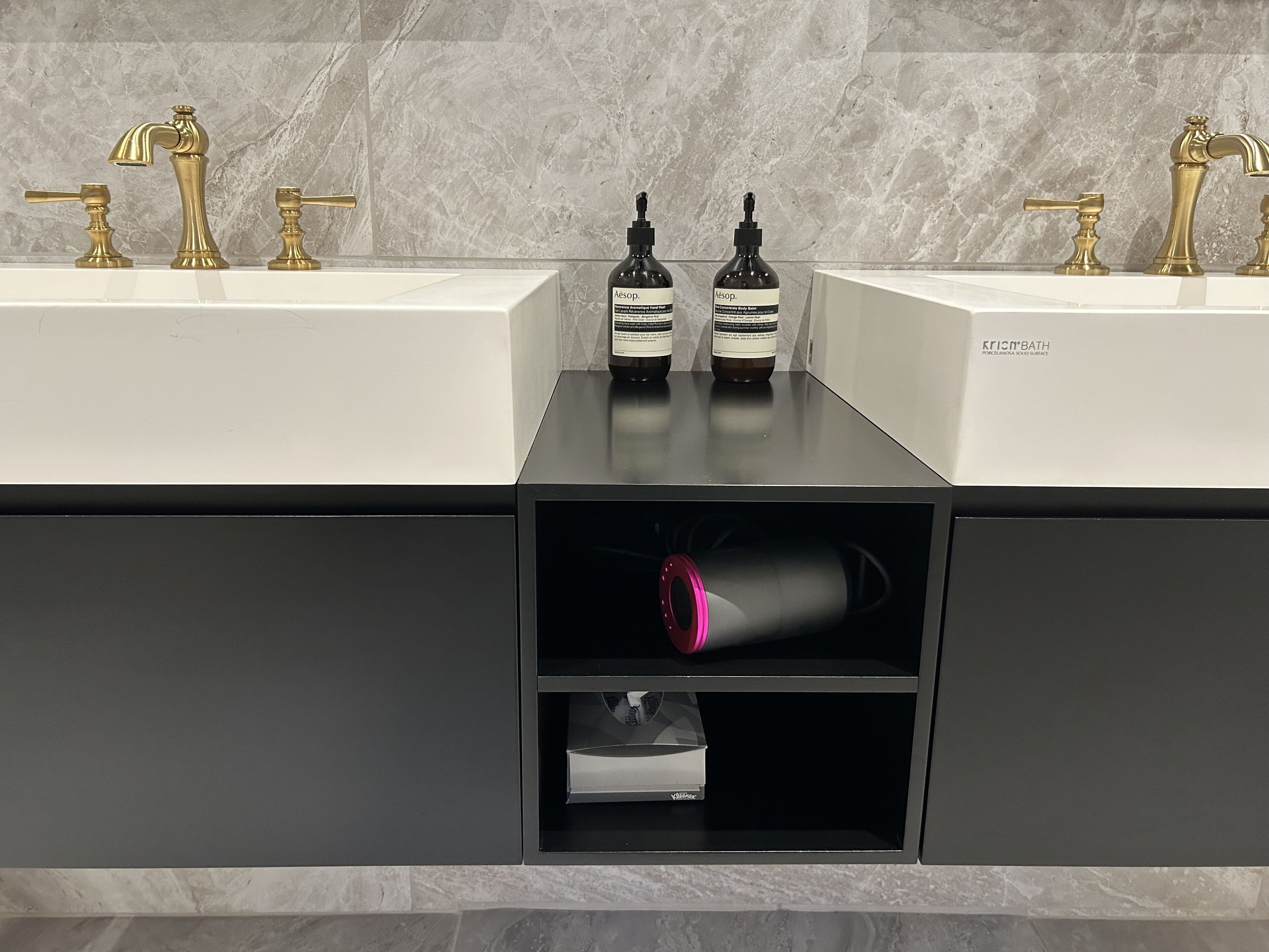 A bathroom with two sinks, each with a gold faucet, and two bottles of Aesop soap on the countertop.
