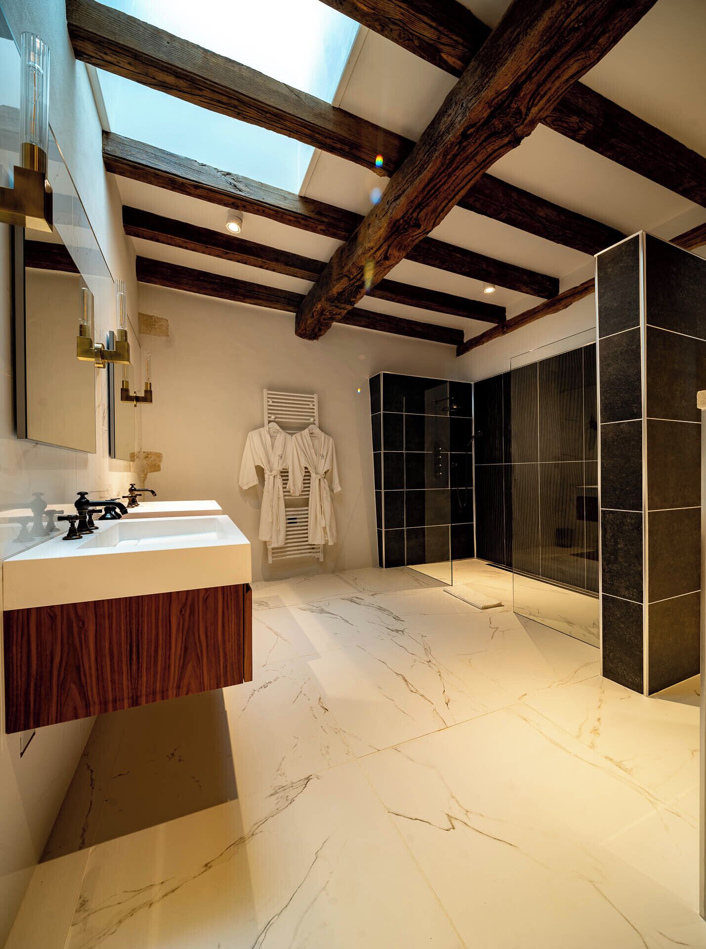 A modern bathroom with a large mirror, a wooden vanity, a glass shower enclosure, and a skylight.