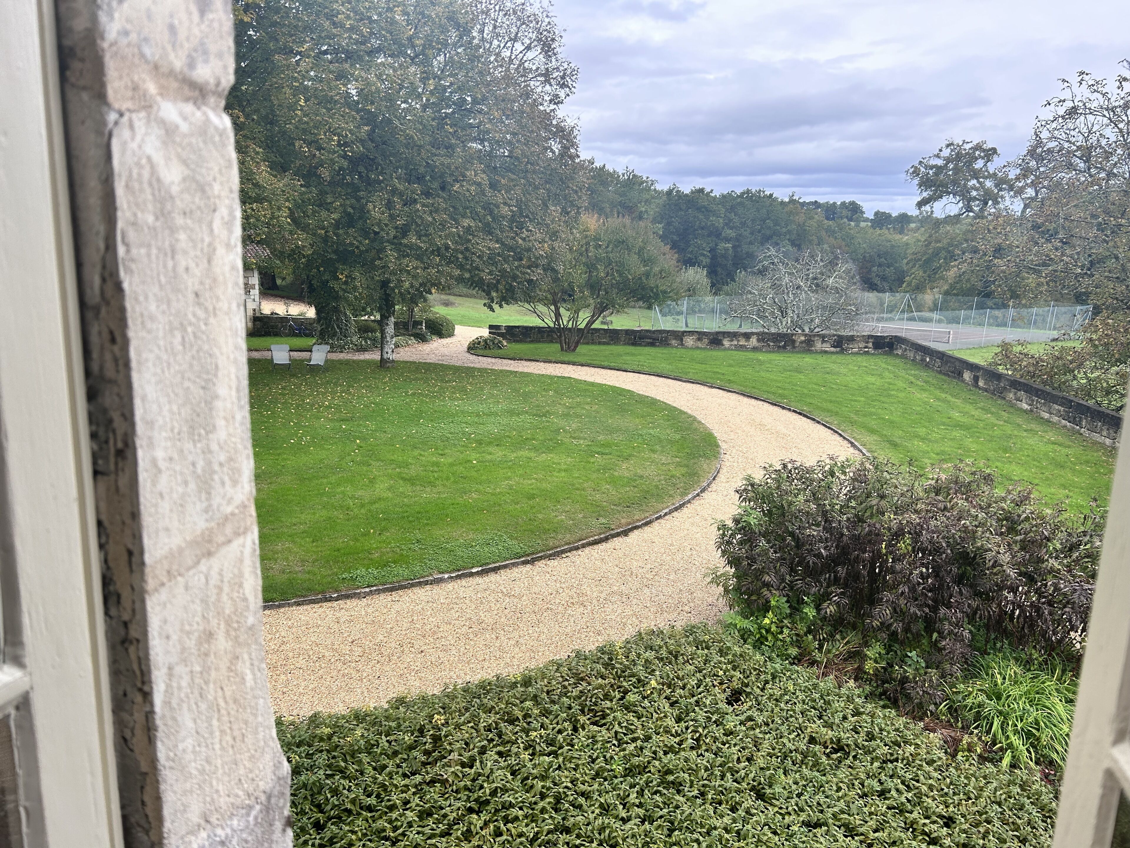 A curved pathway in a park with a grassy area, trees, and a sports field in the background.