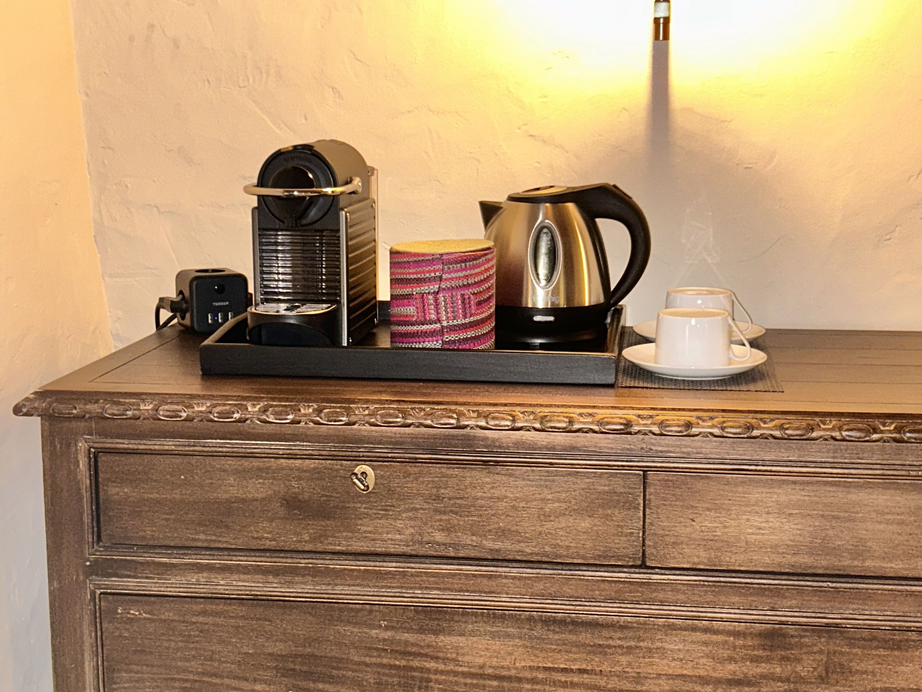 Un aparador de madera con una bandeja que contiene una cafetera, un hervidor, una taza y una xícara.