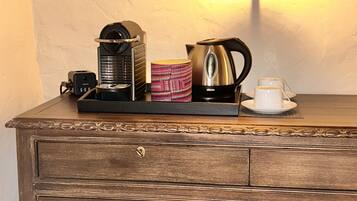 Un aparador de madera con una bandeja que contiene una cafetera, un hervidor, una taza y una xícara.