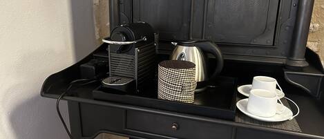 A compact kitchenette with a coffee maker, kettle, and tea set on a black countertop.