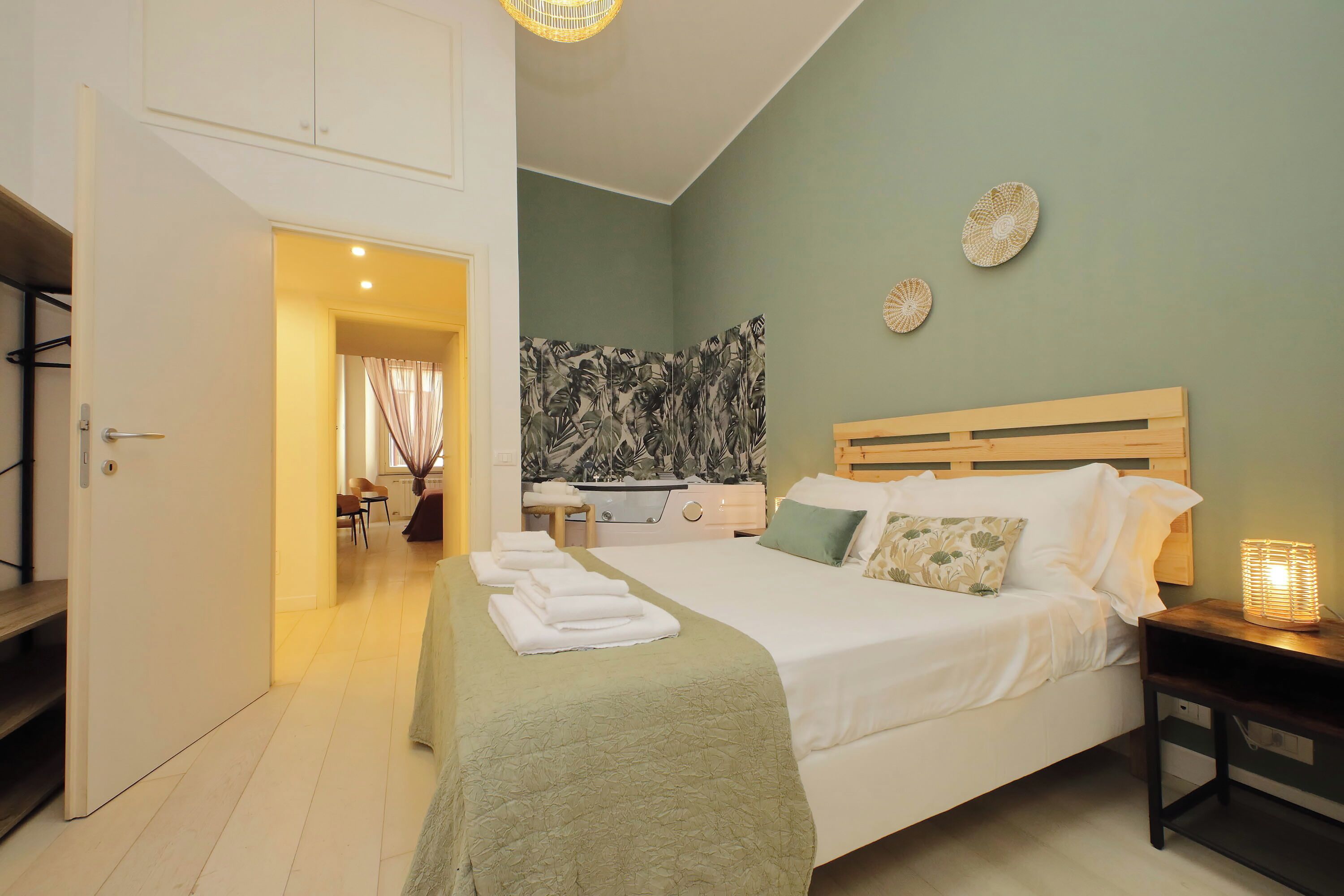 A hotel room with a bed, bedside table, and a view of the dining area.