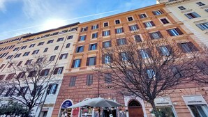 En byggnad med flera våningar, en rad fönster och balkonger, en butiksfasad med en skylt och ett träd i förgrunden.