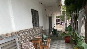 Un espacio de estar al aire libre techado con suelo de baldosas, sillas de metal, una mesa y plantas en macetas.