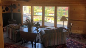 Interior acogedor de una cabaña con chimenea, sofás a rayas, una mesa y ventanas amplias que dan a un paisaje pintoresco.