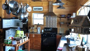 Cocina rústica de cabaña de madera con estufa, refrigerador, ollas colgantes y cafetera.
