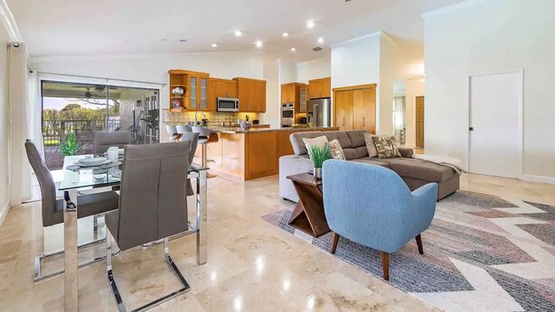 A modern living room with a glass dining table, a sofa, and a ceiling fan.