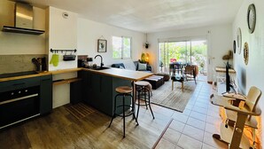 Eine moderne Küche mit Kochinsel, Essbereich mit hohem Tisch und Stühlen sowie Wohnbereich mit Sofa und Couchtisch.