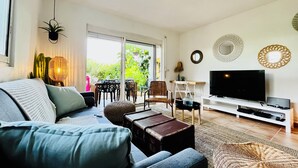 Ein modernes Wohnzimmer mit Sofa, Couchtisch, Fernseher und einem Essbereich mit Stühlen und Tisch.