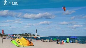 A beach with tents, umbrellas, and a lighthouse in the background. - Condo 300 steps from beach with heated pool and private free parking. (Pompano Beach)