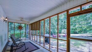 Eine überdachte Veranda mit großen Fenstern, einem Deckenventilator und einem Schaukelstuhl.
