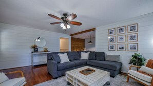 Ein Wohnzimmer mit einem Ecksofa, einem Couchtisch, einem Deckenventilator und gerahmten Bildern an der Wand.