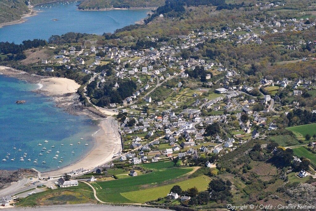 An aerial view of a coastal village with houses, a beach, and boats.